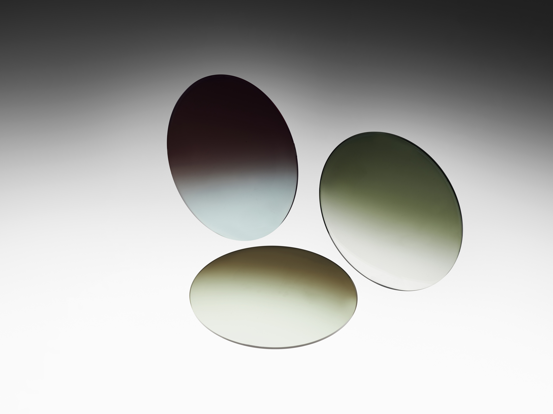 Three round nylon lenses with brown, green, and grey gradient tints, floating over a shaded black and white background.