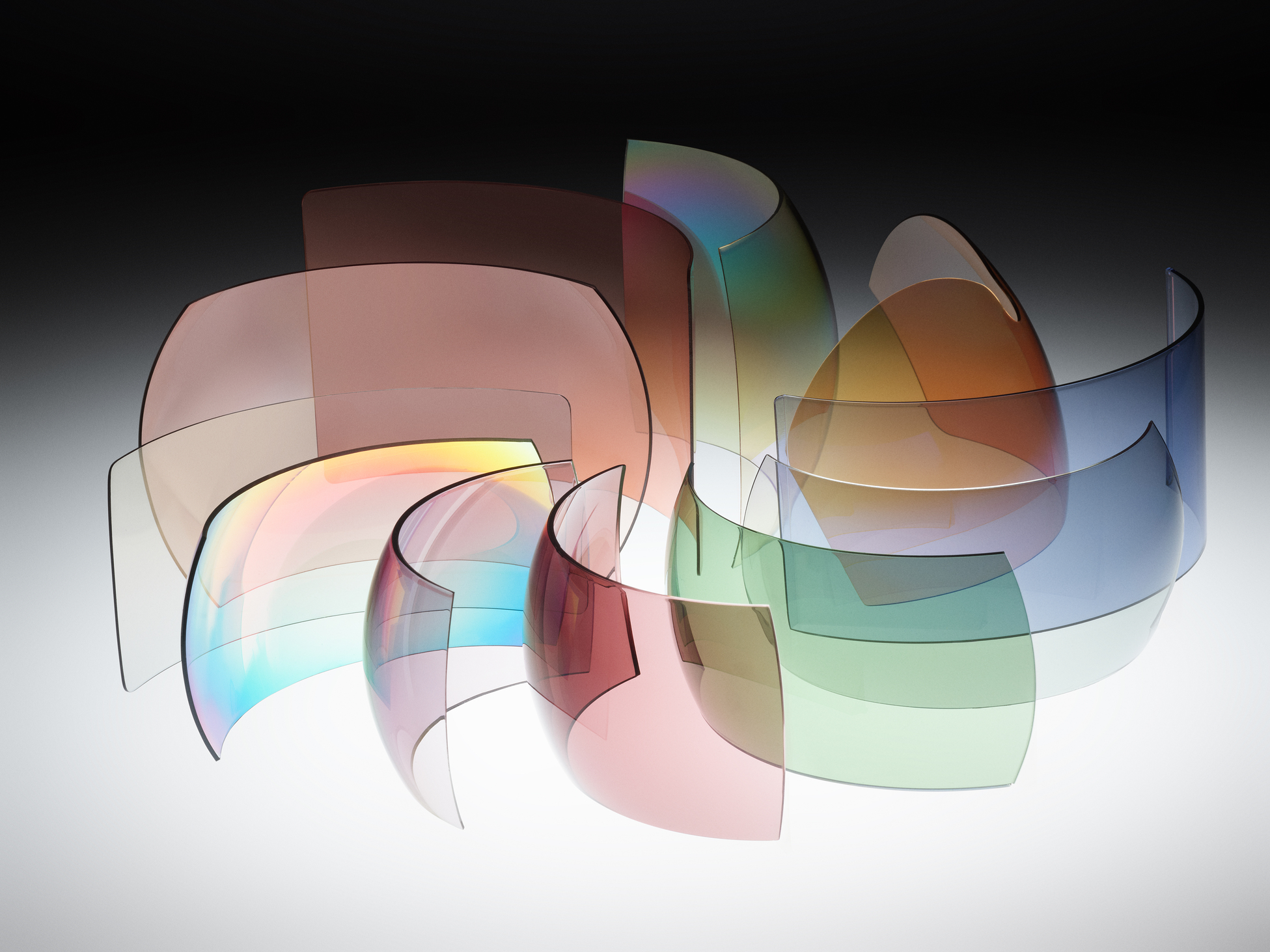 Curved NXT® sunglass lenses arranged in a spiral pattern, showcasing different colors and iridescent reflections.