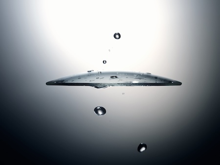 Primo piano di una lente idrorepellente con perfetto effetto goccia dell’acqua, su sfondo grigio sfumato.