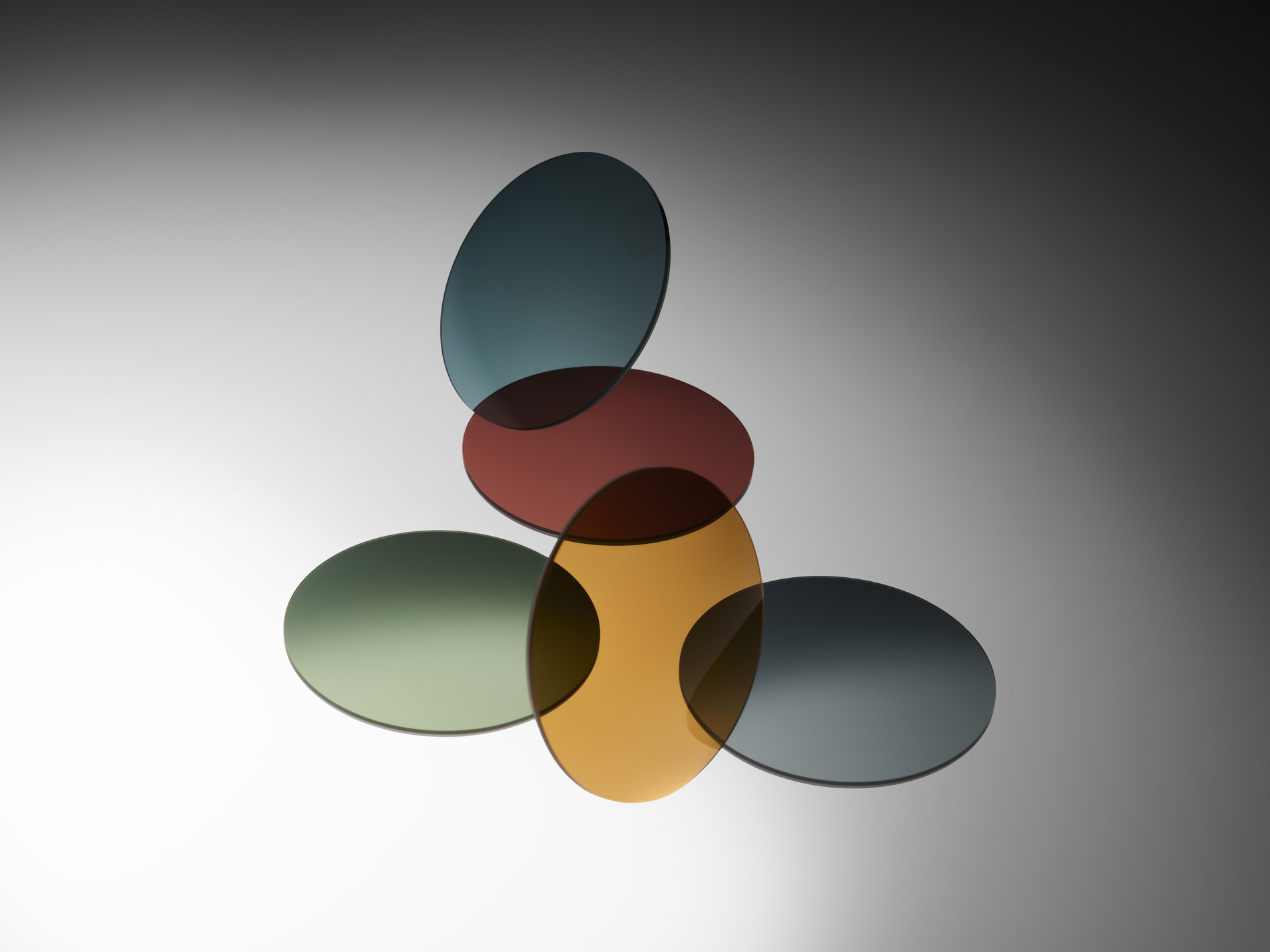Cinque lenti rotonde in vetro premium sovrapposte, in diversi colori, sospese simmetricamente su uno sfondo grigio sfumato.