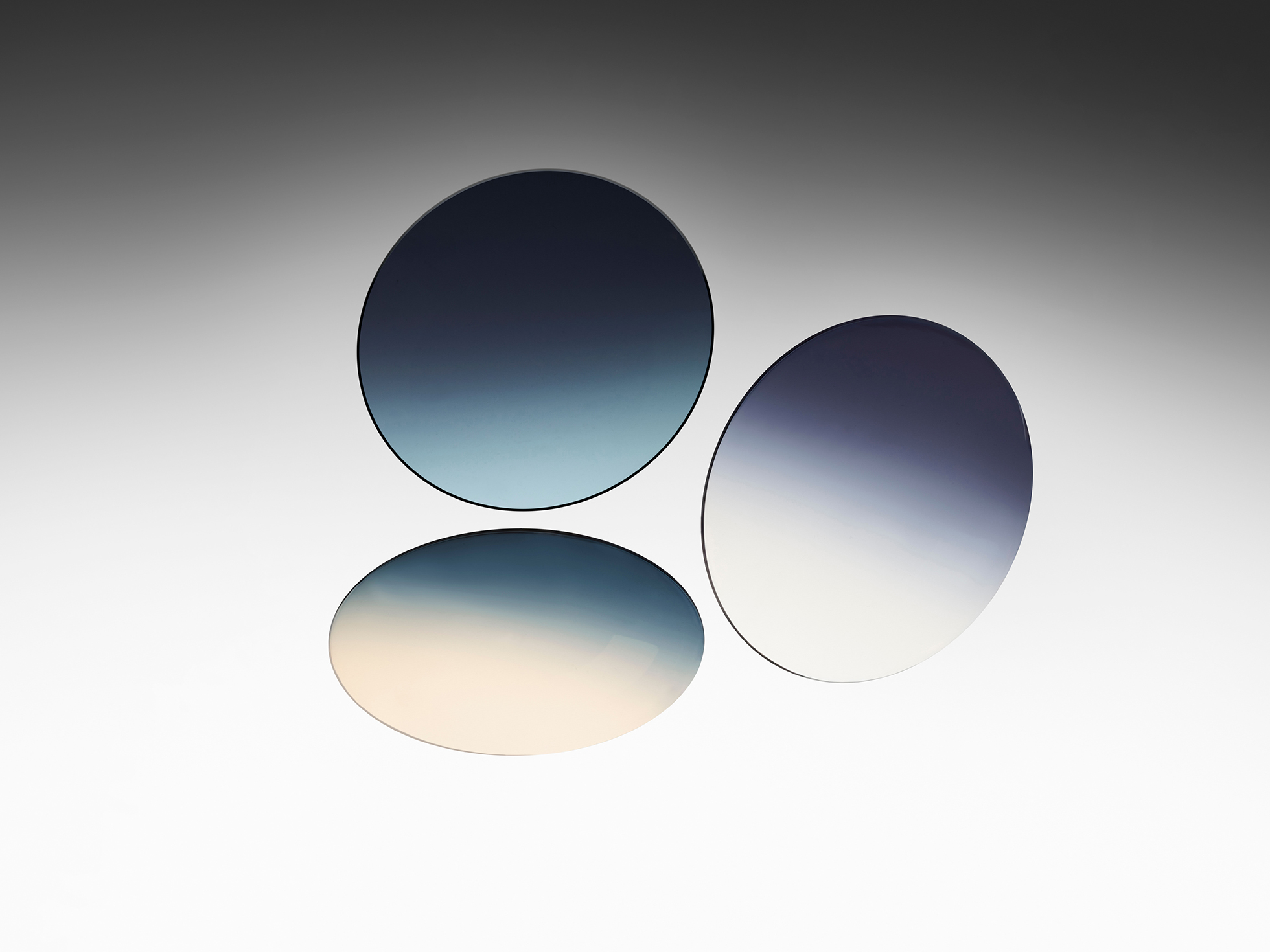 Three round nylon lenses floating against a grey studio background, displaying smooth blue-to-clear gradient tints.