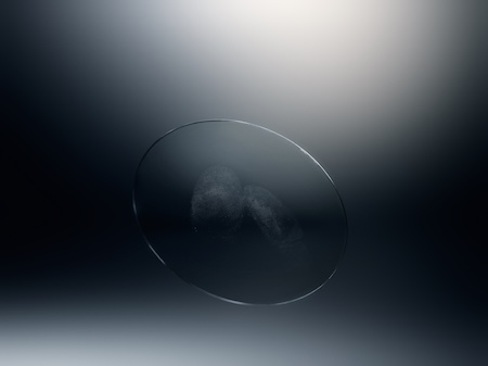 Clear round optical lens revealing faint, minimized fingerprints on its surface against a dark studio gradient background.