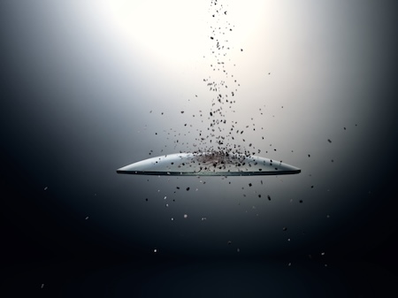Convex optical lens showing particles and fine dust grains bouncing off its treated surface, against a dark studio gradient.