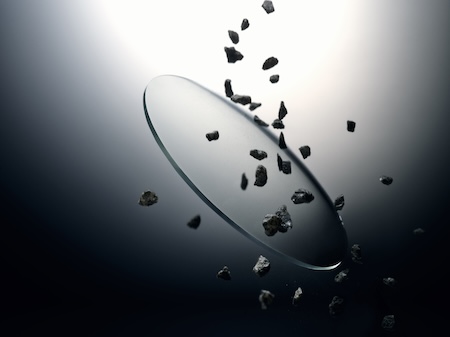 Clear optical lens resisting impact from sharp flying rocks and debris, demonstrating durable anti-scratch coating.